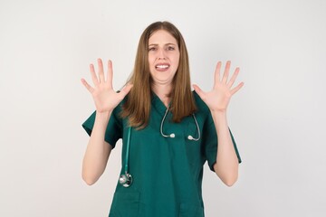 Female doctor wearing a green scrubs and stethoscope afraid and terrified with fear expression stop gesture with hands, shouting in shock. Panic concept.