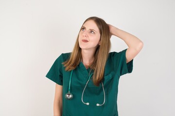 Female doctor wearing a green scrubs and stethoscope confuse and wonder about question. Uncertain with doubt, thinking with hand on head. Pensive concept.