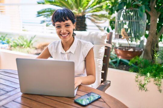 Beautiful woman with short hair sitting at the terrace on a sunny day working from home using laptop