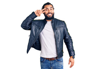 Fototapeta premium Young arab man wearing casual leather jacket doing peace symbol with fingers over face, smiling cheerful showing victory