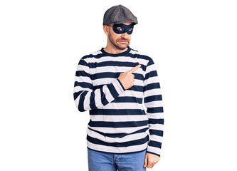 Young handsome man wearing burglar mask pointing aside worried and nervous with forefinger, concerned and surprised expression