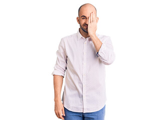 Young handsome man wearing elegant shirt covering one eye with hand, confident smile on face and surprise emotion.