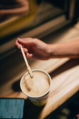 Fototapeta na wymiar A female hand holding a stick over a latte paper mug
