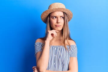 Young beautiful girl wearing summer hat and striped t-shirt thinking concentrated about doubt with finger on chin and looking up wondering