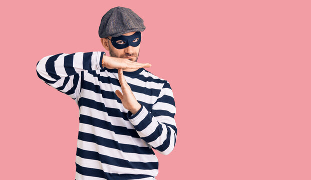Young handsome man wearing burglar mask doing time out gesture with hands, frustrated and serious face