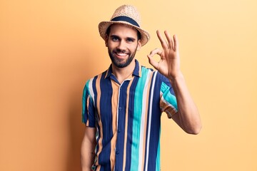 Young handsome man with beard wearing summer hat and shirt smiling positive doing ok sign with hand and fingers. successful expression.