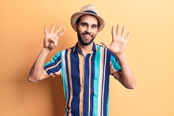 Young handsome man with beard wearing summer hat and shirt showing and pointing up with fingers number nine while smiling confident and happy.