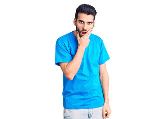 Young handsome man with beard wearing casual t-shirt looking fascinated with disbelief, surprise and amazed expression with hands on chin