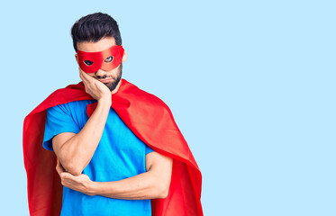 Young handsome man with beard wearing super hero costume thinking looking tired and bored with...