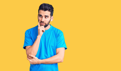 Young handsome man with beard wearing casual t-shirt serious face thinking about question with hand on chin, thoughtful about confusing idea