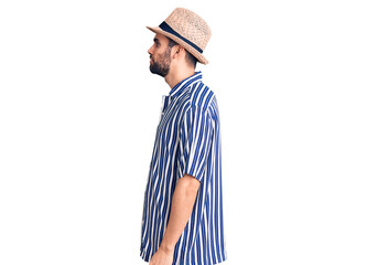 Young handsome man with beard wearing summer hat and striped shirt looking to side, relax profile pose with natural face with confident smile.