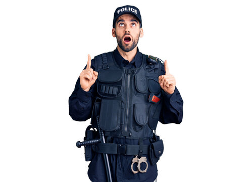 Young handsome man with beard wearing police uniform amazed and surprised looking up and pointing with fingers and raised arms.