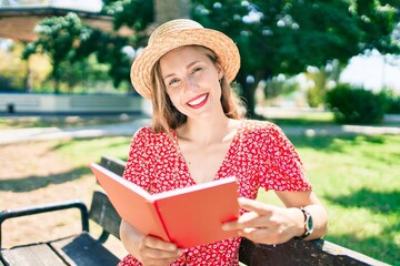 Young blonde woman on vacation reading book sitting on bench at the park