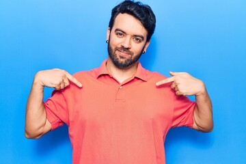 Young hispanic man wearing casual clothes looking confident with smile on face, pointing oneself...