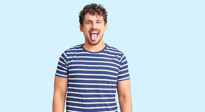 Young handsome man with curly hair wearing casual clothes sticking tongue out happy with funny expression. emotion concept.