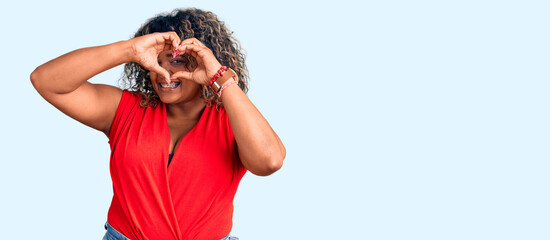 Young african american plus size woman wearing casual style with sleeveless shirt doing heart shape with hand and fingers smiling looking through sign