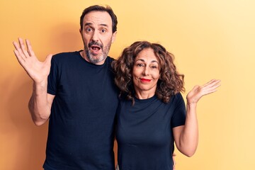 Middle age beautiful couple wearing t-shirt standing over isolated yellow background clueless and...