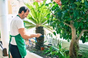 Middle age man with beard smiling happy watering the plants at the terrace