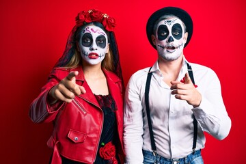 Couple wearing day of the dead costume over red pointing displeased and frustrated to the camera, angry and furious with you