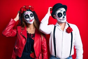 Couple wearing day of the dead costume over red confuse and wondering about question. uncertain with doubt, thinking with hand on head. pensive concept.