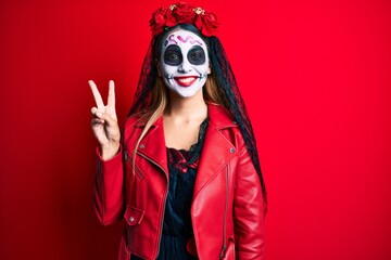 Woman wearing day of the dead costume over red showing and pointing up with fingers number two while smiling confident and happy.