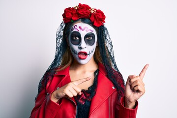 Woman wearing day of the dead costume pointing with fingers to the side in shock face, looking skeptical and sarcastic, surprised with open mouth