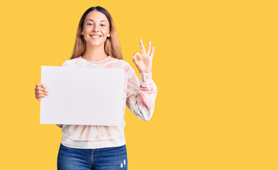 Fototapeta na wymiar Beautiful young woman holding blank empty banner doing ok sign with fingers, smiling friendly gesturing excellent symbol