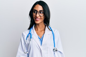 Beautiful hispanic woman wearing doctor uniform and stethoscope looking to side, relax profile pose...