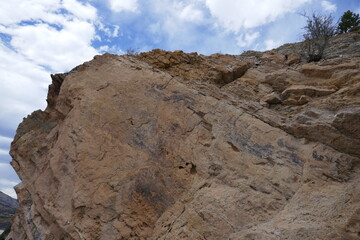 Steep rocky mountainside cliff with blue sky and white clouds overhead