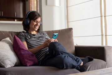 Obraz premium woman sitting on sofa, listening to music while texting