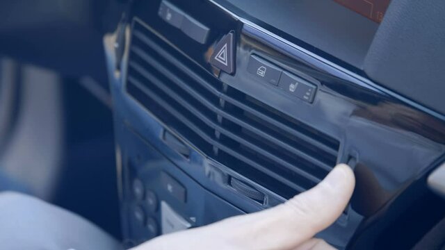 Added shaking from moving the car! The driver's hand controls the direction of movement of ventilation and air conditioning air on a black shiny car dashboard. Closeup