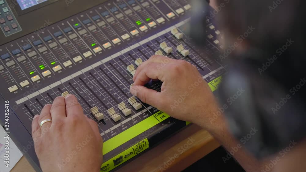 Poster sound engineer moves sliders on digital audio mixer in the control desk of a recording studio produc