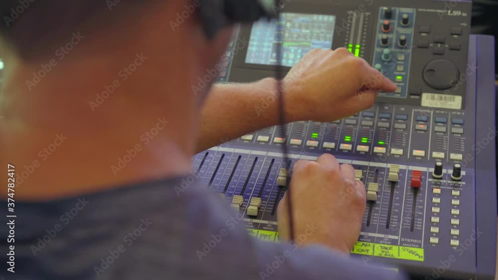 Poster sound engineer moves sliders on digital audio mixer in the control desk of a recording studio produc