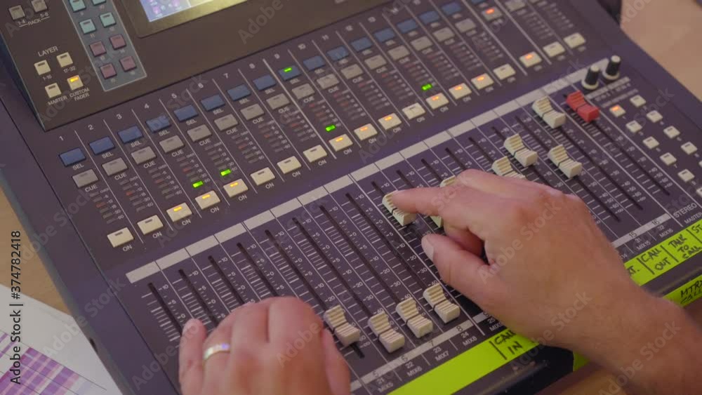 Poster sound engineer moves sliders on digital audio mixer in the control desk of a recording studio produc