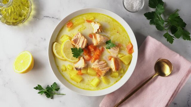Top view of plate with delicious creamy salmon chowder soup on white background with ingredients around. Rotation from right to left side. 4K UHD