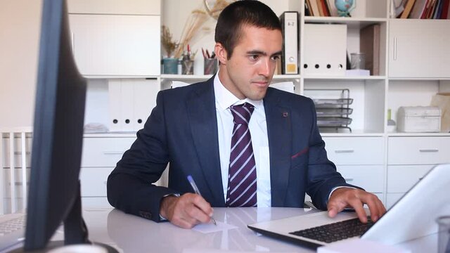 Portrait of successful busy entrepreneur sitting at office desk with papers and laptop 