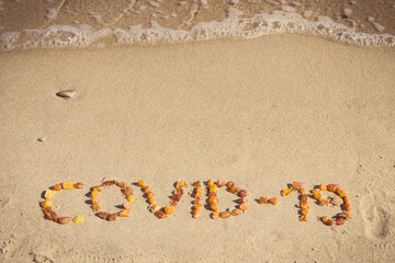 Fototapeta na wymiar Inscription Covid-19 made of amber stones on sand at beach. Holidays and safe during coronavirus