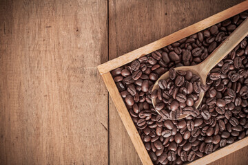Coffee beans roasted in wooden spoon on a pile of black coffee.