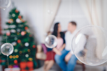 family with a gift at the Christmas tree. the woman, man is sitting on the sofa. new year celebration. wrapped gift