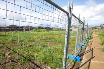 A lot of vacant land guarded by metal construction barrier with some residential suburban houses in...