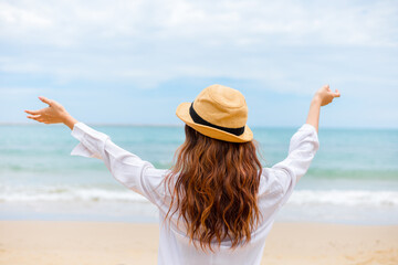 Woman raise hand up on the beach. Happy woman wearing hat.