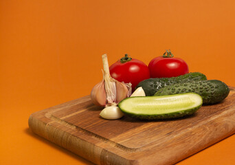 Sliced cucumber, tomatoes and garlic on wooden cutting board. Tomatoes with green ponytails. Healthy food. Copy space. High quality close-up photo