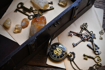 A top view image of an old vintage trunk and pocket watch with citrine crystals and vintage keys. 