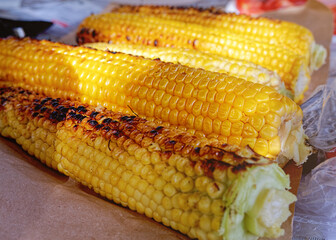 Grilled corn. There are burnt peel and coals on the grain. Seasonal street food, picnic cooking.