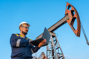 Engineer with a laptop against the background of oil rockers.