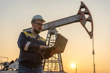 Engineer with a laptop against the background of oil rockers.
