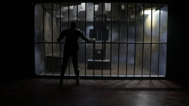 Execution concept. Death penalty guillotine miniature inside old prison. Old prison bars cell lock. Man inside jail. Horror view of Guillotine scale model in the dark