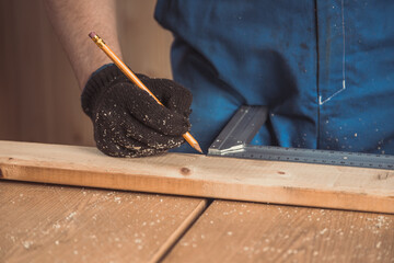 Close up of the man's hand makes a mark on a wooden board with a construction pencil and a...