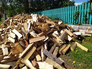 A large pile of chopped wood with an axe in front of the wooden blue house