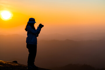 Silhouette of traveler female with camera smart phone and taking photo enjoying in the mountains at Khao Chang Puak mountain Thailand